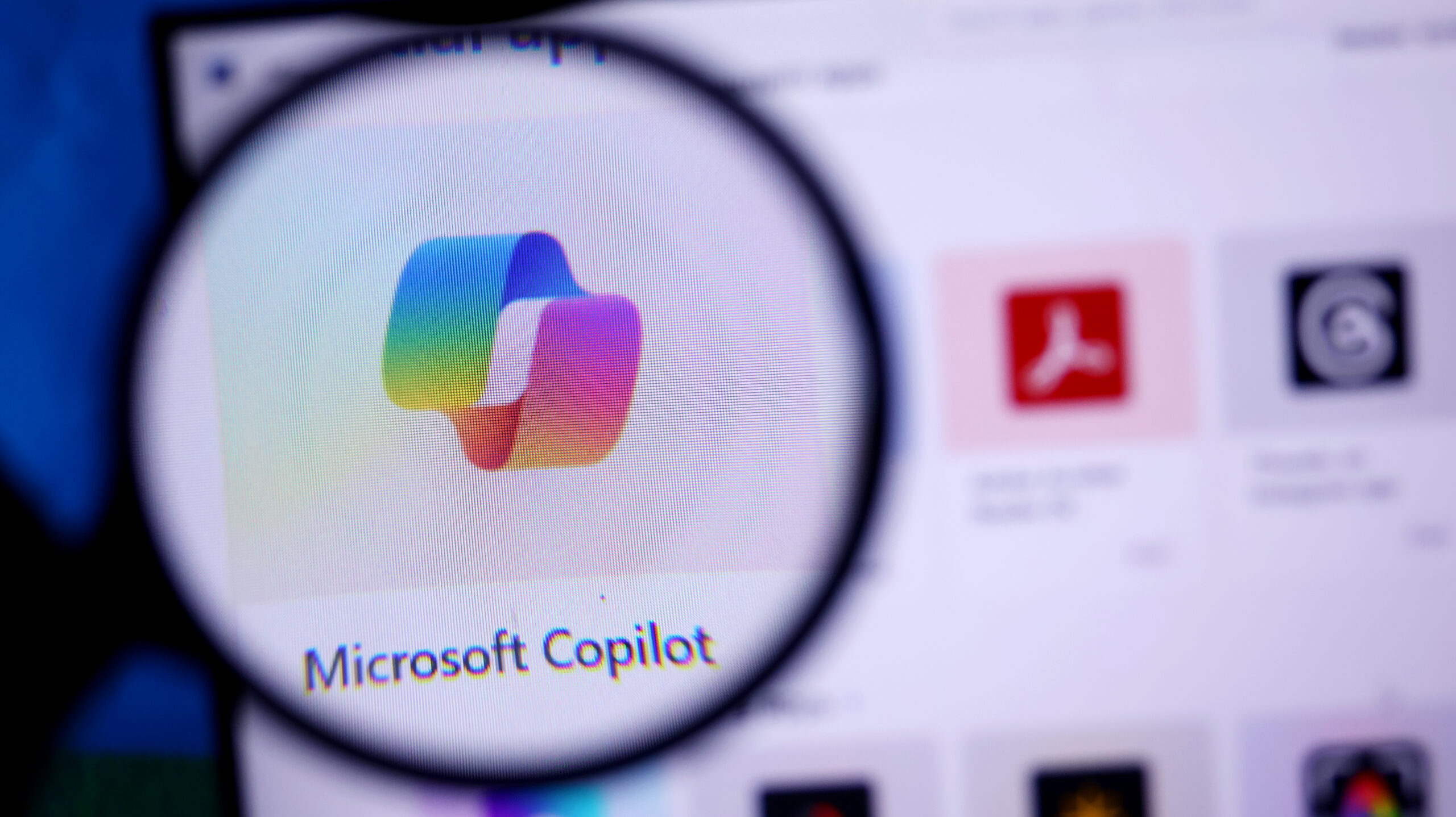 Microsoft Copilot logo viewed through a magnifying glass on a computer screen.